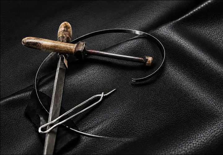 Traditional leather crafting tools — awl, needle, and edge creaser on black leather